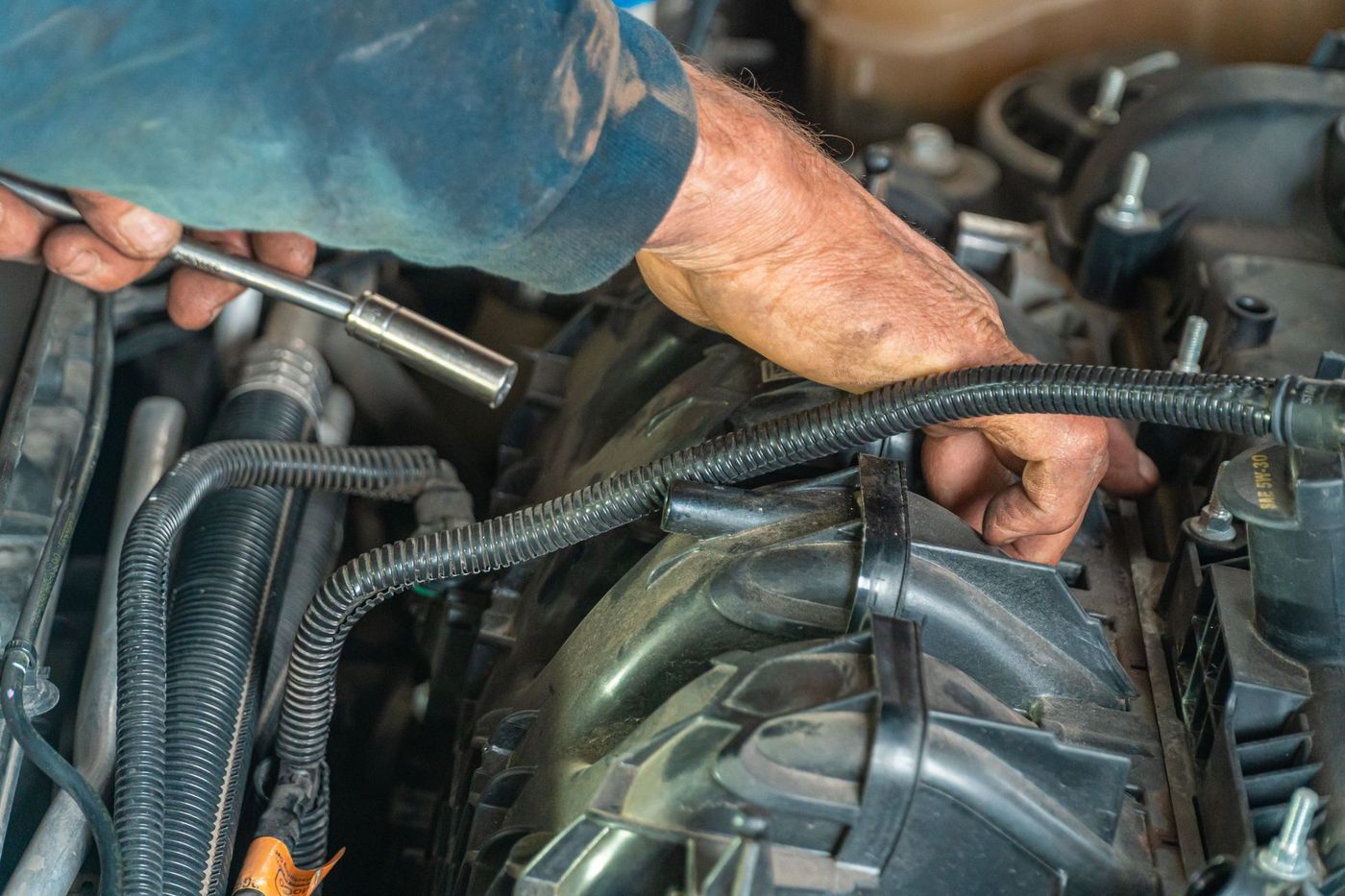 Hands using a socket wrench in an engine bay near the accessory belt