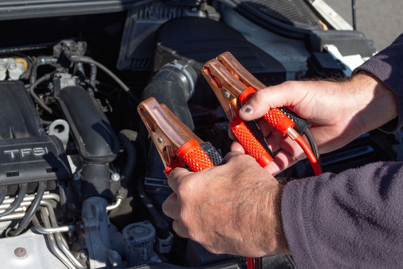 Hands holding jumper cable clamps over an open engine bay