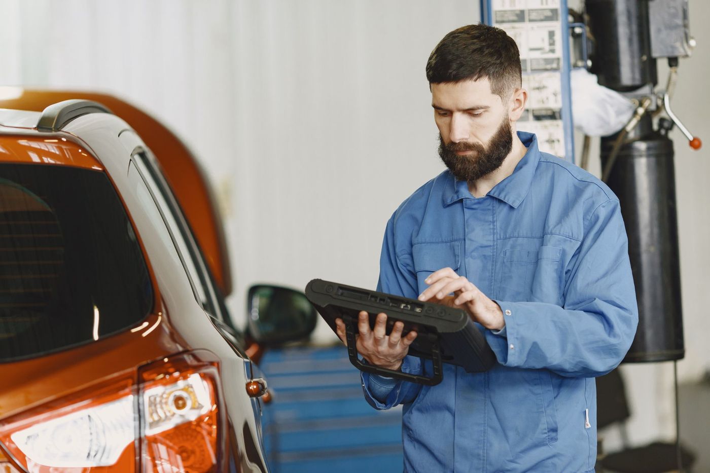 A mechanic reading a diagnostic scan tool beside a vehicle