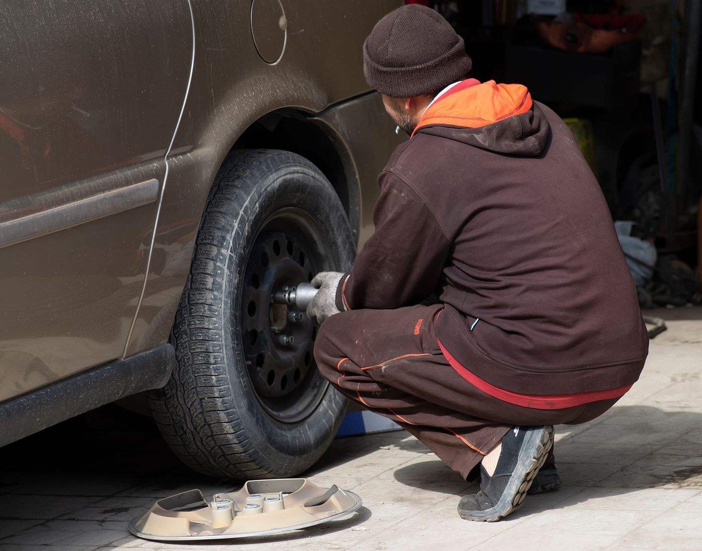 Man kneeling with an impact wrench changing a car wheel on a driveway