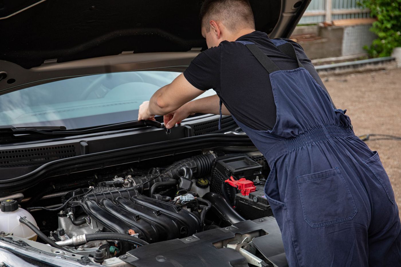 Mechanic in overalls leaning into an open engine bay outdoors